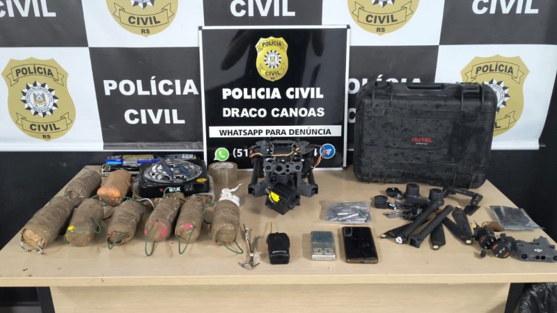 Materiais apreendidos dispostos em uma mesa de fronte a banner da Polícia Civil do Rio Grande do Sul