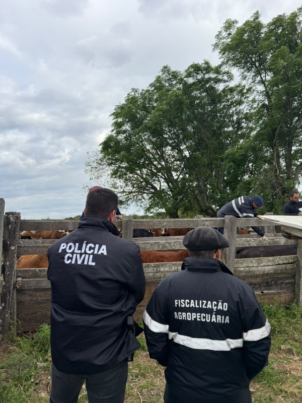 Policial civil e fiscal agropecu&aacute;rio parados de costas com casacos tendo as escritas das respectivas institucionais. Ao fundo, curral com alguns animais